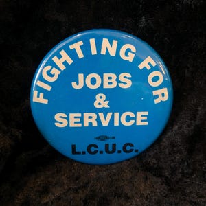 Könnte beinhalten: Blauer Knopf mit weißem Text, der "Fighting for Jobs & Service L.C.U.C." lautet.