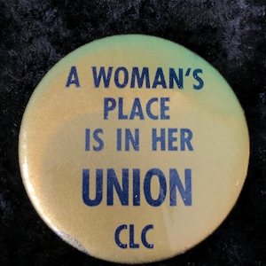 May include: A gold button with the text "A woman's place is in her union CLC" in blue lettering.