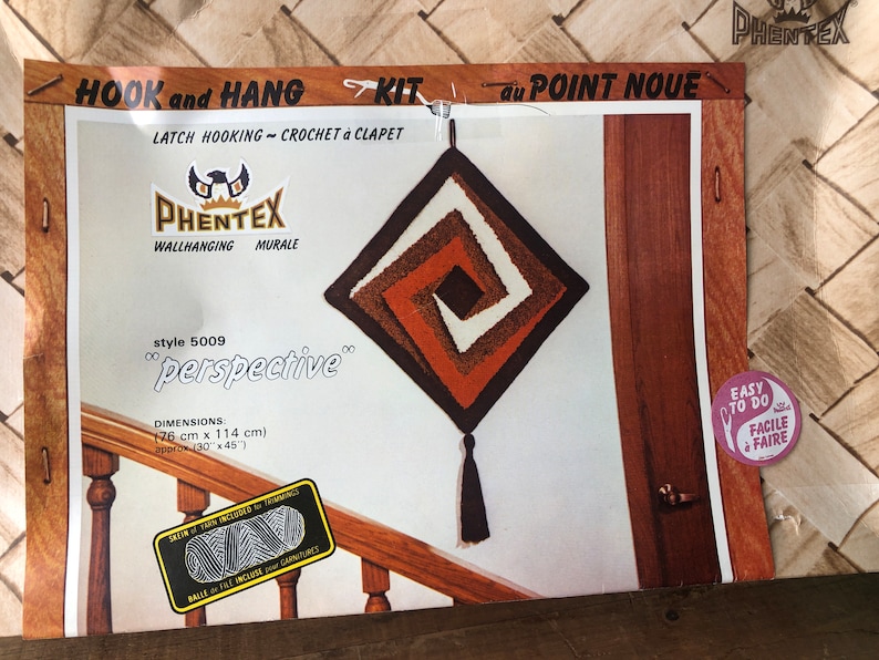 May include: A latch hook kit for a wall hanging called "perspective". The kit includes yarn, instructions, and a latch hook tool. The finished wall hanging is a square with a brown, orange, and white swirl design. The wall hanging is 30 inches by 45 inches.