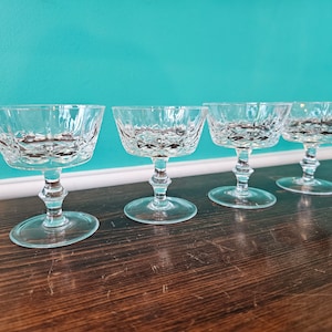 Könnte beinhalten: Vier klare Champagnerkelche aus Glas mit Diamantmuster auf einer dunklen Holzoberfläche.