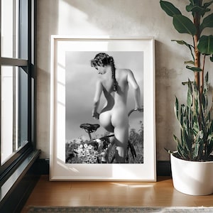 May include: A black and white photograph of a person standing behind a bicycle. The person is nude and has their back to the camera. The bicycle is in the background and is partially obscured by flowers.