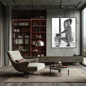 Peut inclure: Une photographie en noir et blanc d'une femme assise sur un rebord de fen&ecirc;tre avec une grande jarre en c&eacute;ramique. La femme est nue et ses cheveux sont tir&eacute;s en arri&egrave;re. La photographie est encadr&eacute;e et accroch&eacute;e &agrave; un mur gris.