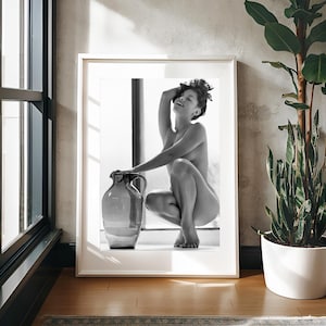 Peut inclure: Une photographie en noir et blanc d'une personne assise avec un grand pot en verre transparent. La personne est assise sur une surface blanche avec une fen&ecirc;tre derri&egrave;re elle.