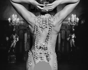 Peut inclure: Une photo en noir et blanc d'une femme portant un collier et une chaîne de corps en perles. La femme est debout, les bras levés au-dessus de sa tête, et son dos est tourné vers l'appareil photo. Le collier et la chaîne de corps sont faits de petites perles scintillantes.