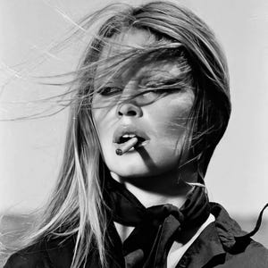May include: Black and white portrait of a woman with long, flowing blonde hair. She wears a dark top and a scarf tied around her neck. A cigarette is held between her lips, and the wind blows through her hair.