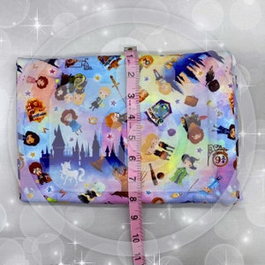 May include: A colorful fabric with a repeating pattern of Harry Potter characters, symbols, and objects. The fabric is approximately 7 inches wide.