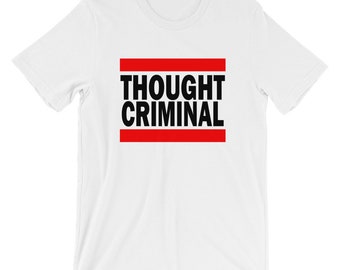 Puede incluir: Camiseta blanca con el texto "THOUGHT CRIMINAL" en letras negras en negrita, enmarcado por dos líneas rojas horizontales. La camiseta tiene cuello redondo y mangas cortas.