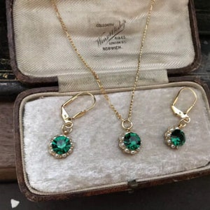 May include: A set of emerald green gemstone earrings and a necklace with a gold chain and a pearl-like border around the gemstones. The jewellery is displayed in a velvet-lined box with the inscription "COLLODONTH, NORWICH".