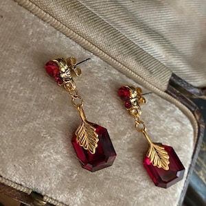 May include: A pair of dangle earrings with red faceted glass stones and gold leaf accents. The earrings are in a small velvet-lined box.