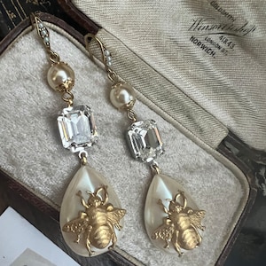 Distintivo cristal transparente de corte esmeralda vintage que presenta una perla artificial ovalada barroca y una perla artificial en forma de lágrima, con una abeja de diseño.