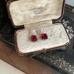Peut inclure: Une paire de boucles d'oreilles en pierres précieuses rouges dans un écrin à bijoux doublé de velours. La boîte est étiquetée "Winsor & Newton 41 & 43 London St. Norwich."
