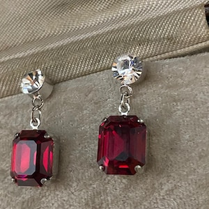 May include: A pair of dangle earrings with a red gemstone and a clear rhinestone at the top.