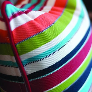May include: A colorful striped pillow with a red, white, green, blue, and pink color scheme. The pillow has a white background with stripes of different colors.