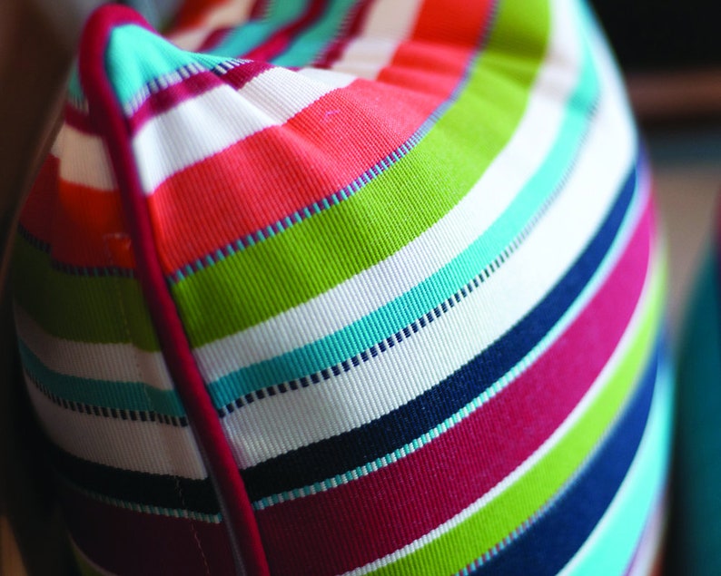 May include: A colorful striped pillow with a red, white, green, blue, and pink color scheme. The pillow has a white background with stripes of different colors.