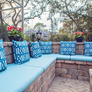 May include: A blue outdoor seating area with a brick wall and blue and white patterned cushions. The seating area is made of brick and has a blue cushion on each seat. The cushions have a geometric pattern in blue and white.