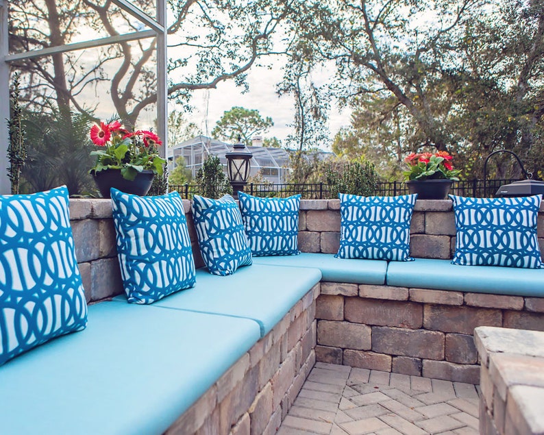 May include: A blue outdoor seating area with a brick wall and blue and white patterned cushions. The seating area is made of brick and has a blue cushion on each seat. The cushions have a geometric pattern in blue and white.