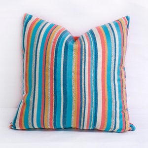 May include: A striped throw pillow with a blue, orange, and pink color scheme. The pillow is made of a soft, textured fabric.