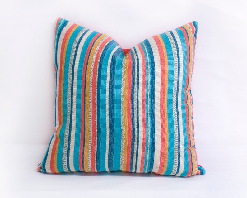 May include: A striped throw pillow with a blue, orange, and pink color scheme. The pillow is made of a soft, textured fabric.