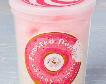 Könnte beinhalten: Ein durchsichtiger Plastikbehälter gefüllt mit rosa Zuckerwatte. Der Behälter hat einen rosafarbenen und weißen Wirbel auf dem Deckel und einen Aufkleber auf der Vorderseite, auf dem "Frosted Donut Cotton Candy" mit einem rosafarbenen Donut-Motiv und den Worten "Chocolate Storybook" in einem Kreis steht.