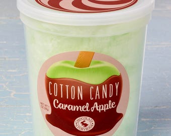Könnte beinhalten: Ein durchsichtiger Plastikbehälter gefüllt mit grünem Zuckerwatte. Der Behälter hat ein rotes und weißes Spiralmuster auf dem Deckel und einen Aufkleber auf der Vorderseite, auf dem "Cotton Candy Caramel Apple" mit einem Logo für Chocolate Storybook steht.