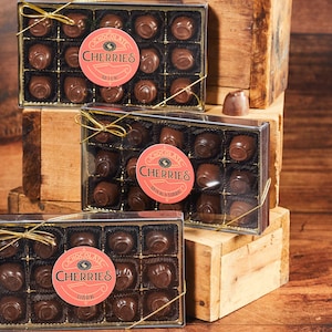 May include: Three boxes of chocolate covered cherries. The top box is labeled "Chocolate Cherries Milk". The middle box is labeled "Chocolate Cherries Milk & Dark". The bottom box is labeled "Chocolate Cherries Dark".