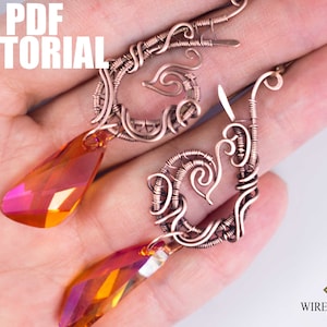 May include: A pair of copper wire earrings with a teardrop-shaped crystal pendant. The earrings are made with intricate wirework and have a delicate, feminine design. The crystals are a vibrant orange-red colour.