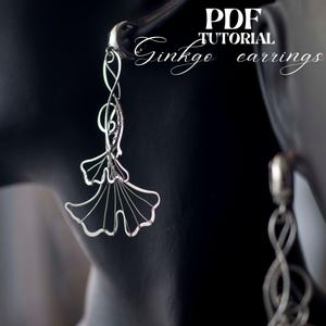 May include: A pair of silver wire earrings shaped like ginkgo leaves. The earrings are hanging from a mannequin's ear. The text "PDF TUTORIAL Ginkgo earrings" is visible in the image.
