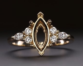 Op de afbeelding: Een gouden ringsetting met een marquise-vormige middelste steen en kleinere ronde en peervormige accentstenen.