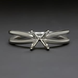 May include: A silver ring setting with a criss-cross design for a center stone.