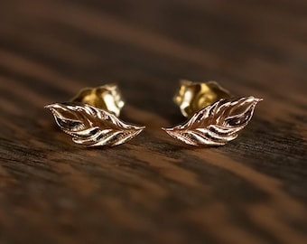 May include: A pair of gold leaf stud earrings. The earrings are small and delicate, with a textured leaf design.