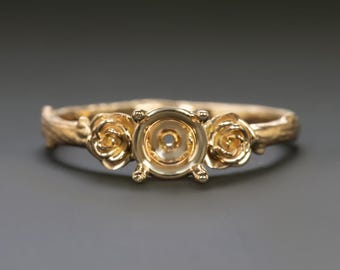 May include: A gold-colored ring with a floral design. The ring features three rose-shaped accents, two on the sides and one at the center, which is designed to hold a gemstone. The band has a textured, organic appearance.