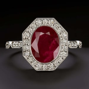 May include: A silver ring with a large oval ruby center stone. The ruby is surrounded by a halo of small diamonds, set in an octagonal shape. The band features additional diamond accents.