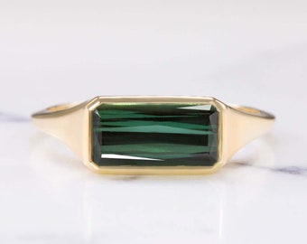 May include: A gold ring featuring a rectangular, emerald-green gemstone. The ring has a simple, elegant design with a polished gold band. The gemstone is set in a bezel setting, enhancing its color and clarity. This piece is suitable for everyday wear or special occasions.