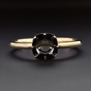May include: A gold ring with a black setting for a round gemstone. The setting has a square shape with small black accents around the edge.
