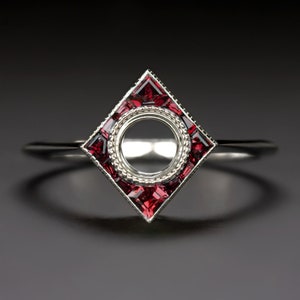 May include: A silver ring with a square setting featuring a circle for a stone. The setting is surrounded by small red gemstones.