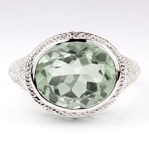 May include: A silver ring with a large, round, light green gemstone set in a bezel setting. The ring has a textured band with smaller gemstones.