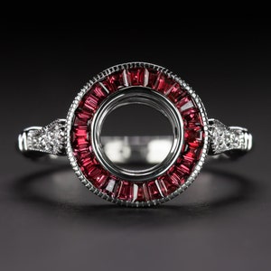 Op de afbeelding: Een zilveren ring met een ronde zetting omgeven door een halo van rode baguette-vormige edelstenen. De ring heeft een delicate band met kleine diamanten aan weerszijden van de zetting.