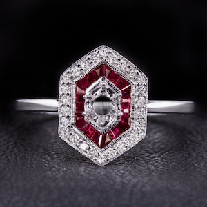 May include: A hexagonal ring setting with a centre stone and a halo of small diamonds. The halo is surrounded by a row of red rubies.