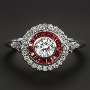 May include: A silver ring with a large round diamond center stone surrounded by a halo of smaller diamonds and a ring of red rubies.