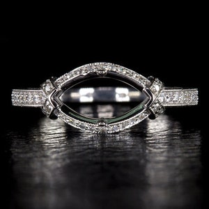 Könnte beinhalten: Ein silberner Ring-Sockel mit einer Marquise-förmigen Fassung für den Mittel-Stein. Die Fassung ist mit kleinen Diamanten um den Mittel-Stein und auf der Ringschiene verziert.