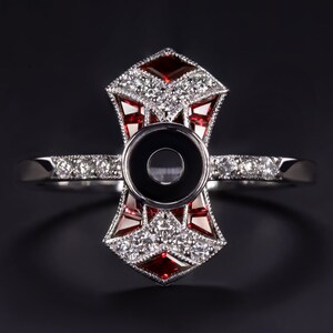 May include: A silver ring with a geometric design featuring red and white stones. The ring has a large centre setting that is empty, ready for a gemstone.