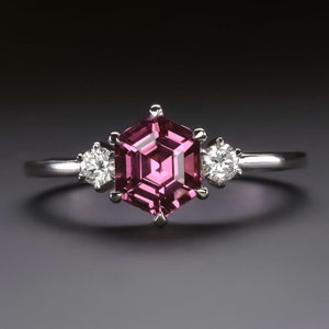 May include: A silver ring with a pink hexagonal gemstone and two smaller round diamonds on either side.