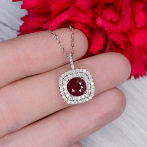 May include: A silver necklace with a square pendant featuring a large red ruby surrounded by a double halo of smaller diamonds.