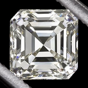 Puede incluir: Un diamante claro de talla cuadrada con una superficie multifacética. La gema está sujeta por una herramienta plateada sobre un fondo negro. Las facetas del diamante reflejan la luz, creando una exhibición brillante.