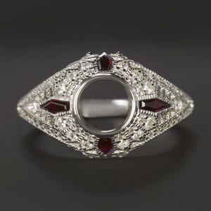 May include: A silver ring with a round setting for a gemstone. The ring is decorated with small diamonds and red gemstones.