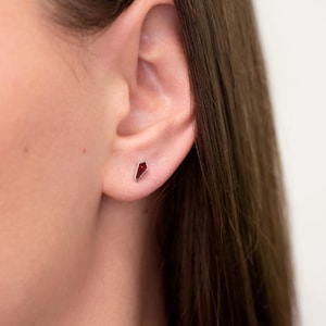 May include: A close-up of a person's ear with a small, red, geometric-shaped stud earring.