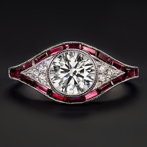May include: A silver ring with a large round diamond center stone surrounded by a halo of baguette-cut rubies. The ring has a delicate, vintage-inspired design.