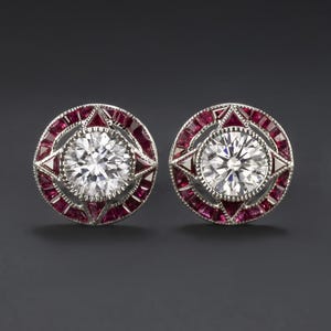 May include: A pair of silver earrings with a round, clear diamond center surrounded by a halo of red rubies.