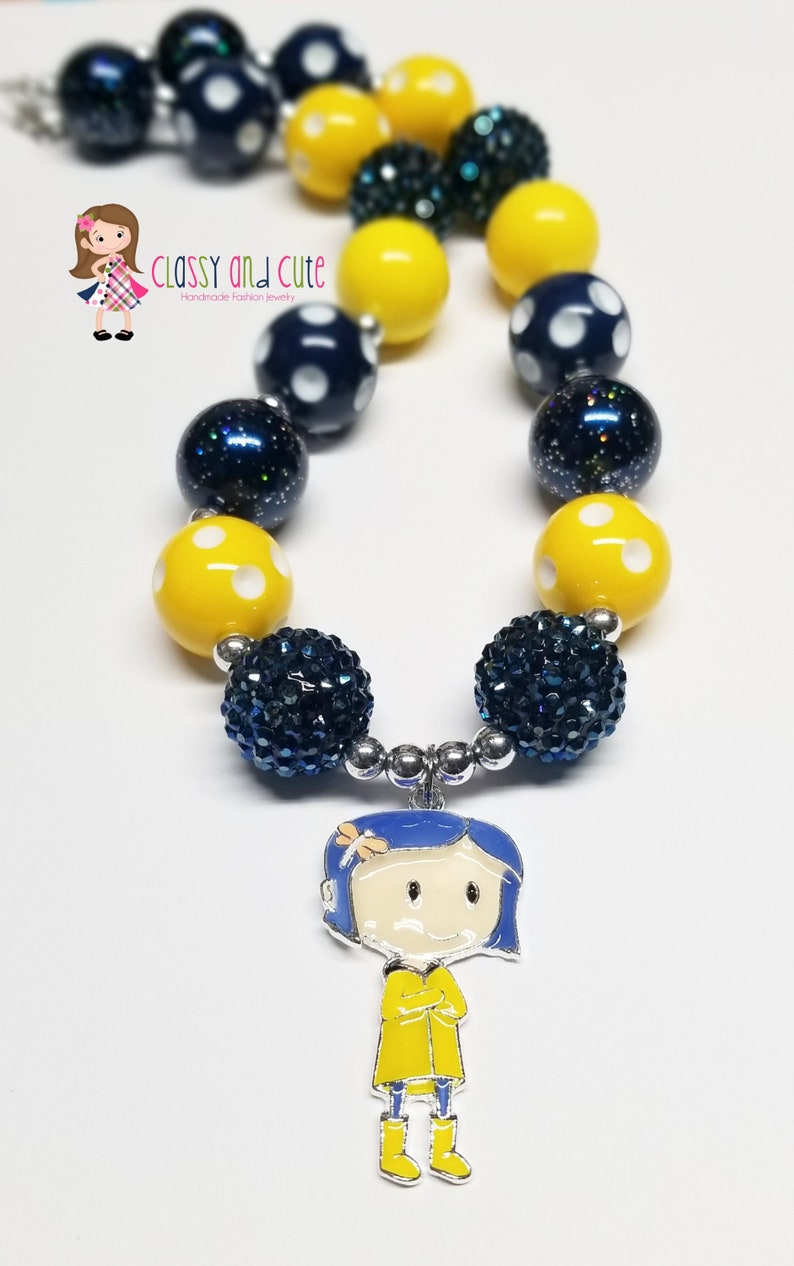 May include: A necklace featuring yellow and blue beads, some with white polka dots, and a charm of a girl in a yellow raincoat. The necklace is made of chunky beads and has a silver clasp.