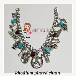 May include: A silver charm bracelet with a rhodium plated chain and various charms, including a horseshoe, a cross, a cowboy boot, and a cowboy hat. The charms are accented with turquoise blue beads.
